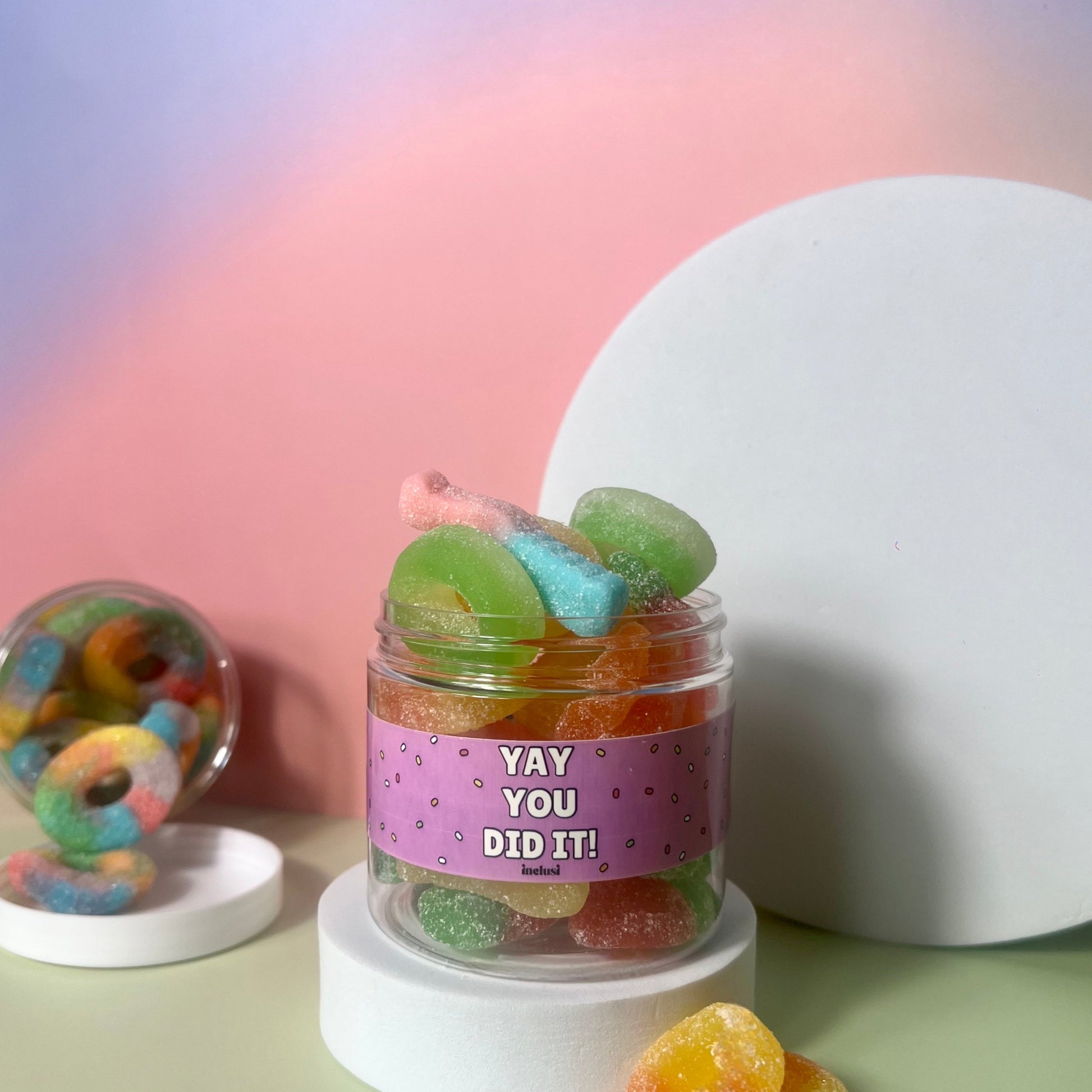 Jar of colourful vegan and gluten free gummy candies with a 'YAY YOU DID IT!' label on a pastel background