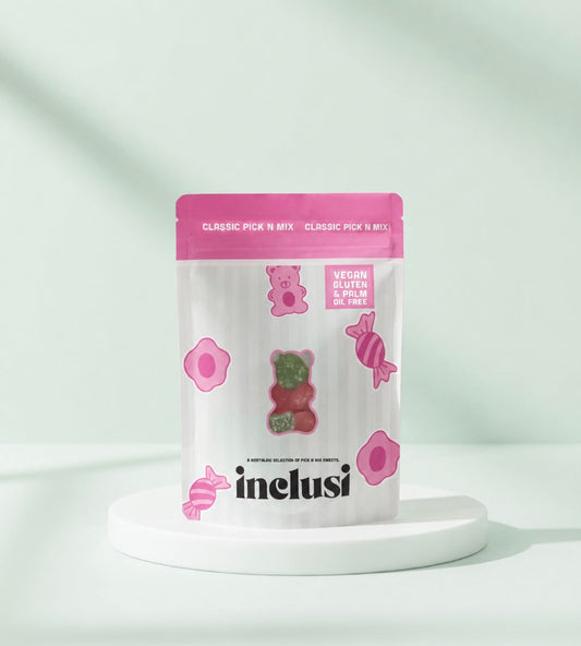 A stand-up pouch of inelusi Classic Pick N Mix gummy candies displayed on a white round pedestal against a clean, light green background with soft leaf shadows.